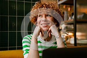Cheerful middle-aged woman using laptop while sitting in cafe indoors