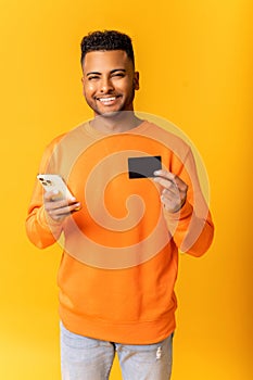 Cheerful middle-eastern guy is using smartphone and credit card for shopping online. Happy indian man is ordering food