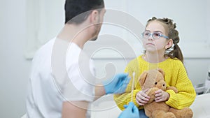 Cheerful Middle Eastern pediatrician distracting cute Caucasian girl taking Covid test. Positive doctor calming down