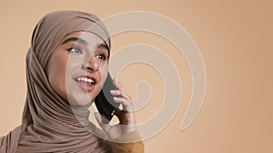 Cheerful Middle-Eastern Woman Talking On Cellphone Looking Aside, Beige Background