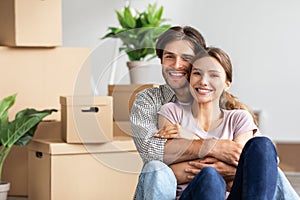 Cheerful millennial caucasian guy hugging woman sit among boxes, plants, rest from packing belongings