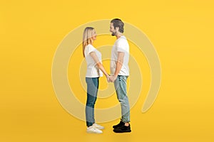 Cheerful millennial caucasian male and female in white t-shirts holding hands, looking at each other