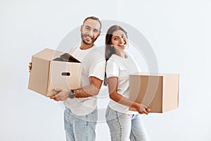 Cheerful millennial couple carrying cardboard boxes, packing stuff for relocation