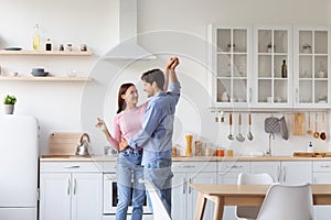 Cheerful millennial european husband and wife have fun and dancing in modern kitchen interior