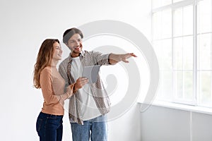 Cheerful millennial european male and female planning new interior with tablet in empty room of new apartment