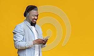 Cheerful millennial guy listening music on smartphone with wireless headphones