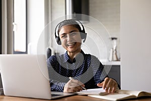 Cheerful millennial hindu female studying from home using laptop earphones