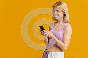 Cheerful millennial lady using smartphone, surfing internet or scrolling social networks feed, yellow background, banner