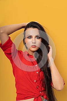 Cheerful mixed race brunette in red blouse isolated on yellow background. Beauty surprised woman with long dark hair and