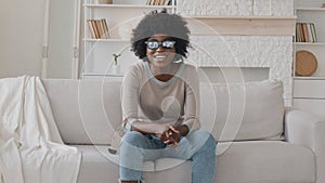 Cheerful mixed race girl wearing 3d glasses having fun enjoy free time relaxing on comfy sofa holding remote control