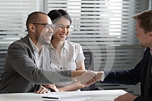 Cheerful mixed race married spouse shaking hands with real estate agent.