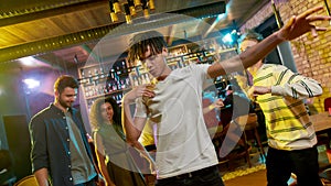 Cheerful mixed race young man dancing at party in the bar. Friends celebrating, having fun in the background