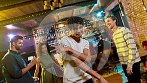 Cheerful mixed race young man posing at camera, dancing at party in the bar. Friends celebrating, having fun in the