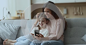 Cheerful mom and cute daughter girl watching content on smartphone