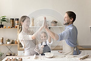 Cheerful mom, dad and little daughter baking in home kitchen