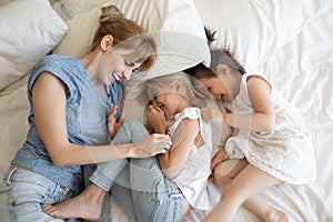 Cheerful mom and daughters relaxing on bed