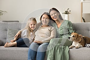 Cheerful mom, grandma, happy girl and dog resting on couch
