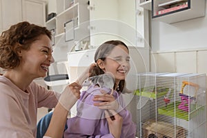 Cheerful mom and teenage daughter laughing playing with rat pet