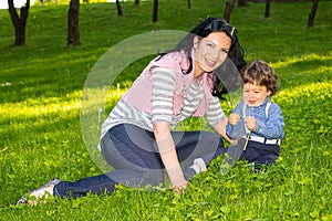 Cheerful mother and boy sit in grass