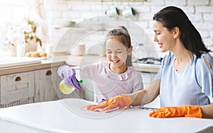 Cheerful mother and daughter cleaning table surface together