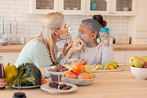 Cheerful mother and daughter playing tricks while cooking