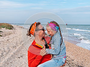 Cheerful mother and daughter smiling walking on sea beach. Happy family. Cute little child playing rainbow pop it toy