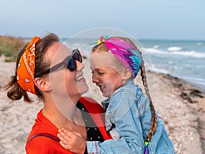 Cheerful mother and daughter smiling walking on sea beach. Happy family. Cute little child playing rainbow pop it toy