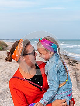 Cheerful mother and daughter smiling walking on sea beach. Happy family. Cute little child playing rainbow pop it toy