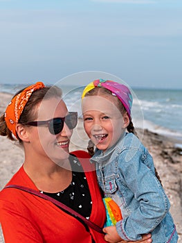 Cheerful mother and daughter smiling walking on sea beach. Happy family. Cute little child playing rainbow pop it toy