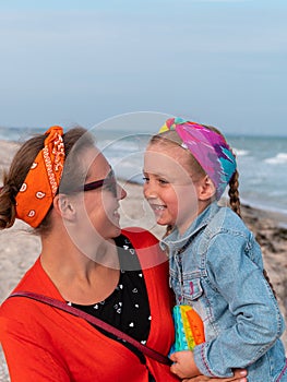 Cheerful mother and daughter smiling walking on sea beach. Happy family. Cute little child playing rainbow pop it toy