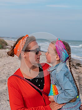 Cheerful mother and daughter smiling walking on sea beach. Happy family. Cute little child playing rainbow pop it toy