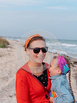 Cheerful mother and daughter smiling walking on sea beach. Happy family. Cute little child playing rainbow pop it toy