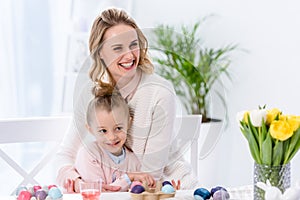 Cheerful mother and daughter by table with painted eggs