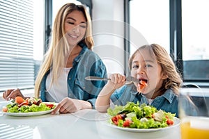 Cheerful mother and daughter tasting salad in kitchen