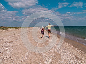 Cheerful mother and daughter walking running on sea beach. Happy family. Cute little child playing with mom outdoors