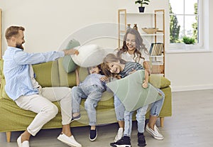 Cheerful mother, father and children fighting with pillows on couch in living room