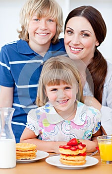 Cheerful mother and her children eating waffles