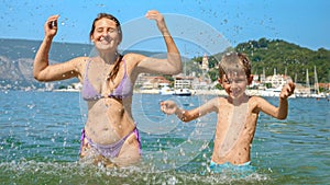 Cheerful mother and her son playing and splashing water at the sea beach. Family holiday, vacation, and the carefree