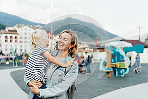 A cheerful mother hugs her daughter and laughs while holding her in her arms. Happy candid emotions.