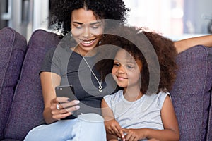 Cheerful mother little daughter spending time at home using smartphone