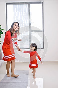 Cheerful mother little daughter standing in living room at home moving dancing to favourite song together