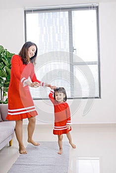 Cheerful mother little daughter standing in living room at home moving dancing to favourite song together