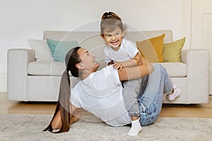 Cheerful mother playing with her little daughter in living room