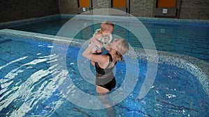 A cheerful mother plays with a small child in the indoor pool for children.