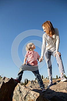Cheerful mother and son are standing on large stones, holding hands, looking at each other. Unusual perspective