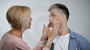 Cheerful mother wiping mouth to irritated adult son, overprotection effect
