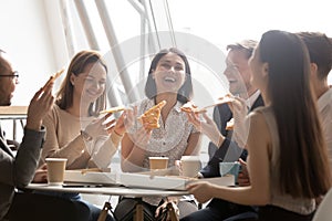 Cheerful multicultural team workers laugh share lunch meal eating pizza