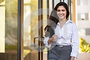 Cheerful multiethnic business woman walking to work smiling, with electronic tablet, Indian, hispanic, south asian