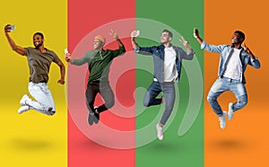 Cheerful multiethnic guys jumping and taking selfie on smartphones over colorful backgrounds