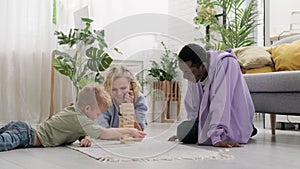 cheerful multiracial family having fun, playing wooden block tower game together on the carpet at home.
